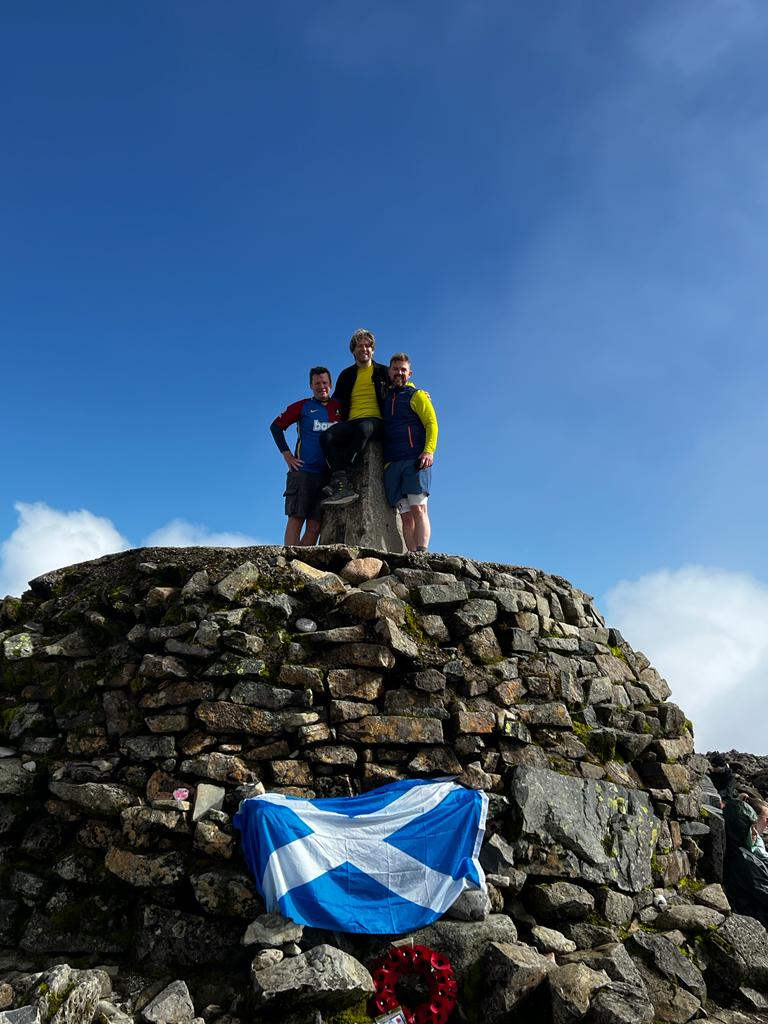 Three men standing on top of a Scottish peak