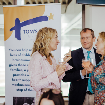 Three people speaking in front of a Tom's Trust roller banner