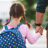 Little girl with pigtails holding dads hand walking to school